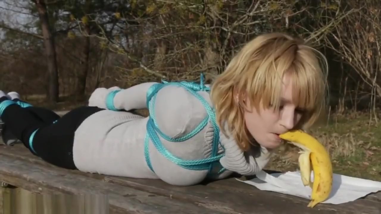 Cute girl eats banana while tied outside
